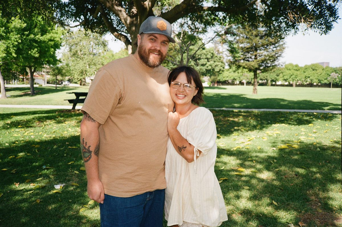 Matt and Kim smiling together under a tree in a park.